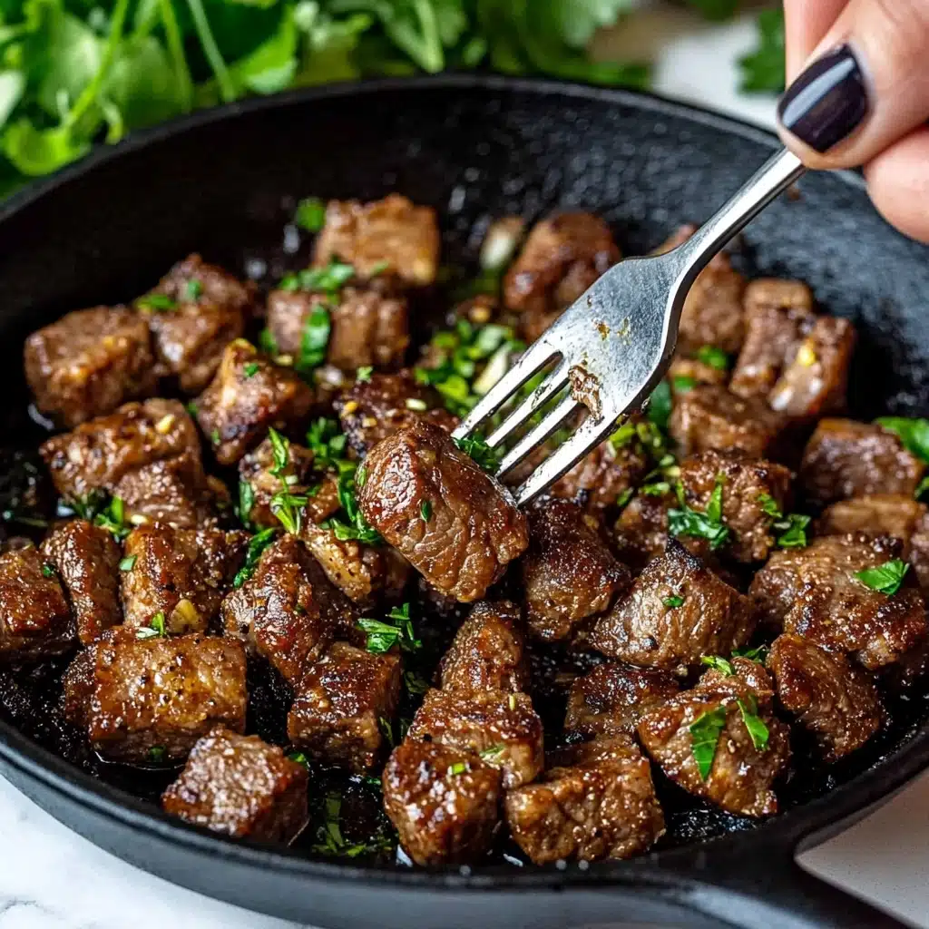 Garlic Butter Steak Bites, Quick Steak Bites, Easy Steak Dinner, Juicy Steak Bites, Tender Steak Appetizer A close-up of browned meat cubes in a black cast iron pan, each piece sprinkled with chopped green herbs and small bits of garlic, showing a mix of crispy and tender textures; a woman's hand with dark painted nails holds a silver fork piercing one meat cube, the background softly blurred with green leaves, and the pan sits on a white marbled surface.