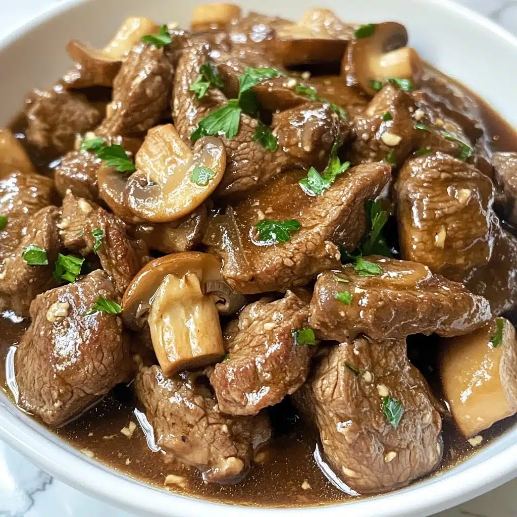 Instant Pot Garlic Butter Steak Bites, quick beef recipes, how to make steak in Instant Pot, tender steak bite ideas, easy Instant Pot dinner The dish shows small brown pieces of cooked meat mixed with sliced mushrooms and bits of garlic, all covered in a thin brown sauce. It is garnished with small green parsley leaves scattered on top. The food is served in a white bowl, sitting on a white marbled surface. The close-up angle reveals the texture of the meat and mushrooms clearly.