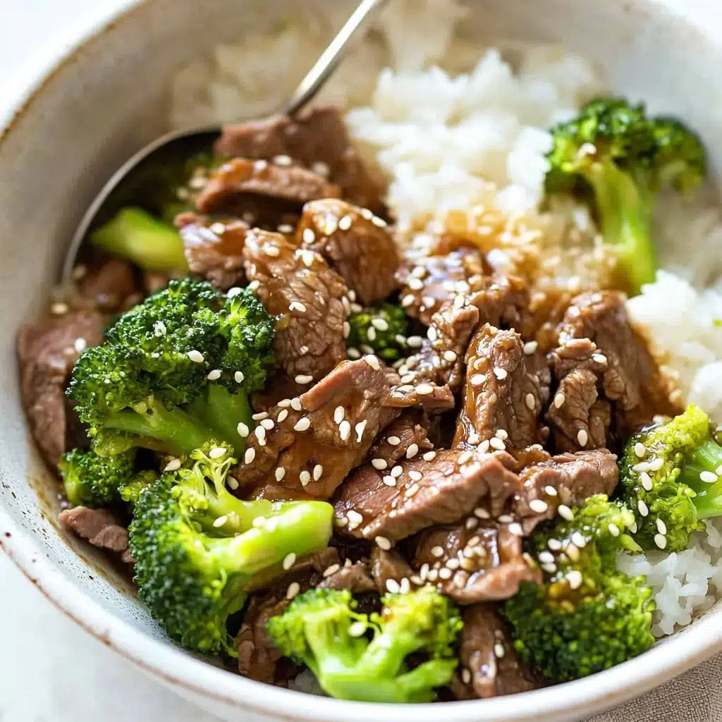 Chinese Beef and Broccoli, Chinese Beef and Broccoli recipe, Easy Chinese Beef and Broccoli, Beef and Broccoli stir-fry, Homemade Chinese Beef and Broccoli A bowl filled with white rice at the bottom, topped with bright green broccoli florets and slices of cooked brown beef mixed with sauce, sprinkled with white sesame seeds. The broccoli pieces are vibrant and fresh-looking, while the beef slices are thin and tender, creating a textured and colorful contrast over the rice. A silver spoon rests inside the bowl, slightly buried in the food. The bowl is white, and it sits on a white marbled surface.