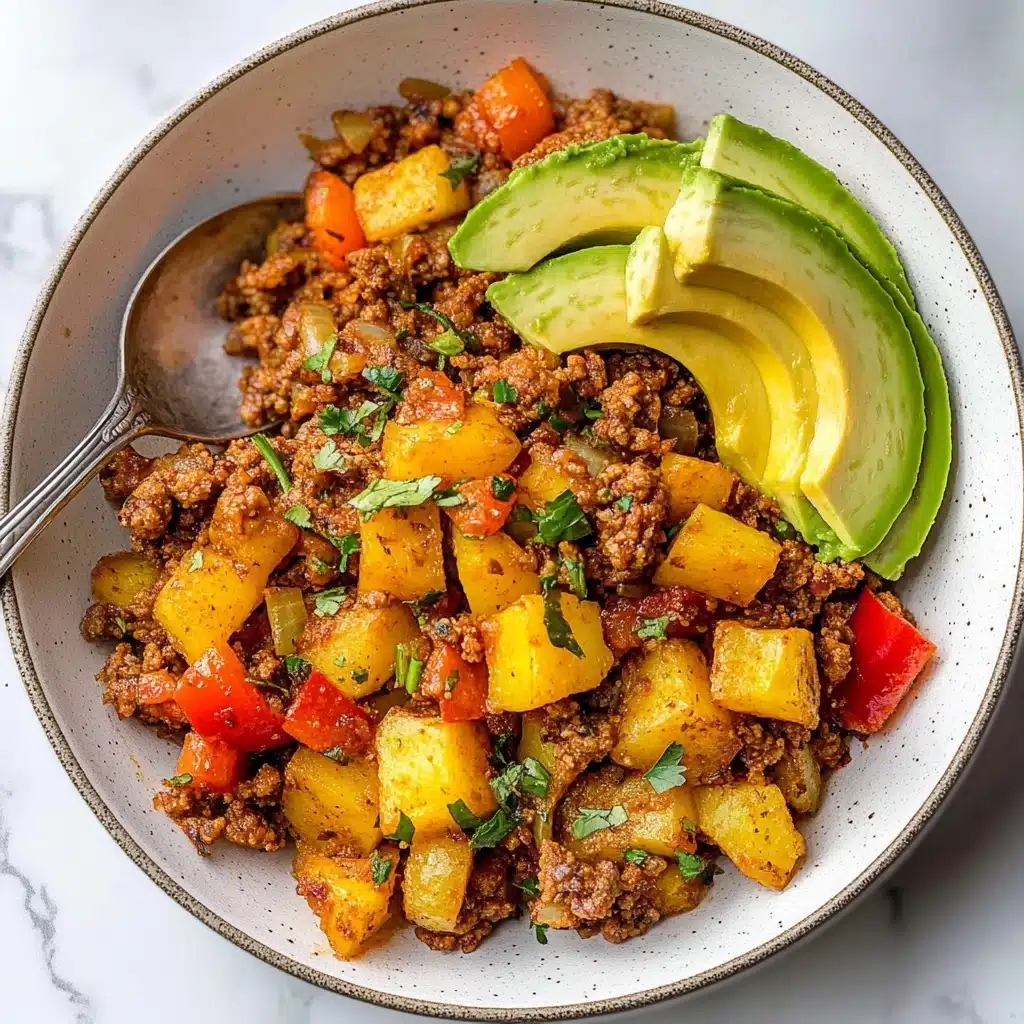Mexican Ground Beef and Potato Skillet, easy Mexican dinner, quick ground beef recipes, one-pan beef and potato skillet, family-friendly weeknight meal A white bowl filled with three main layers of food: the bottom layer has small chunks of browned ground meat mixed with diced cooked yellow potatoes, all seasoned and slightly crispy. The middle layer includes bright red bell pepper pieces and translucent, cooked onion bits scattered throughout. The top layer has three slices of fresh avocado, light green in color, placed on one side of the bowl and sprinkled lightly with green herbs. The bowl is set on a white marbled surface with a silver spoon resting inside the bowl.