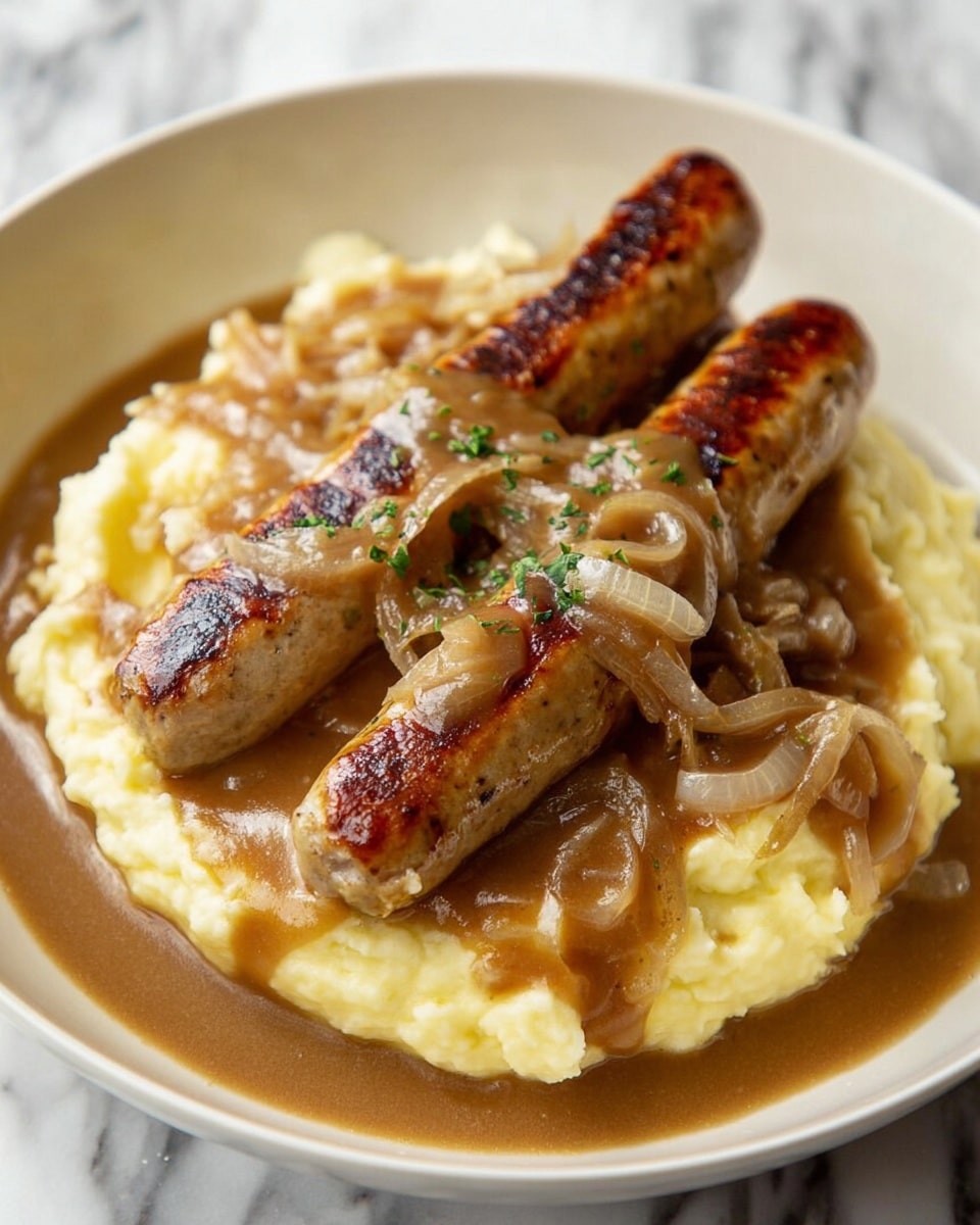 A white plate holds a serving of creamy pale yellow mashed potatoes as the bottom layer. Two browned sausages with charred spots rest on top of the mashed potatoes. The sausages are covered with a thick brown gravy that includes soft, translucent cooked onion slices spread generously over the sausages and potatoes. A woman's hand with a silver spoon is reaching into the plate near the edge of the mashed potatoes. The plate sits on a white marbled surface. photo taken with an iphone --ar 4:5 --v 7