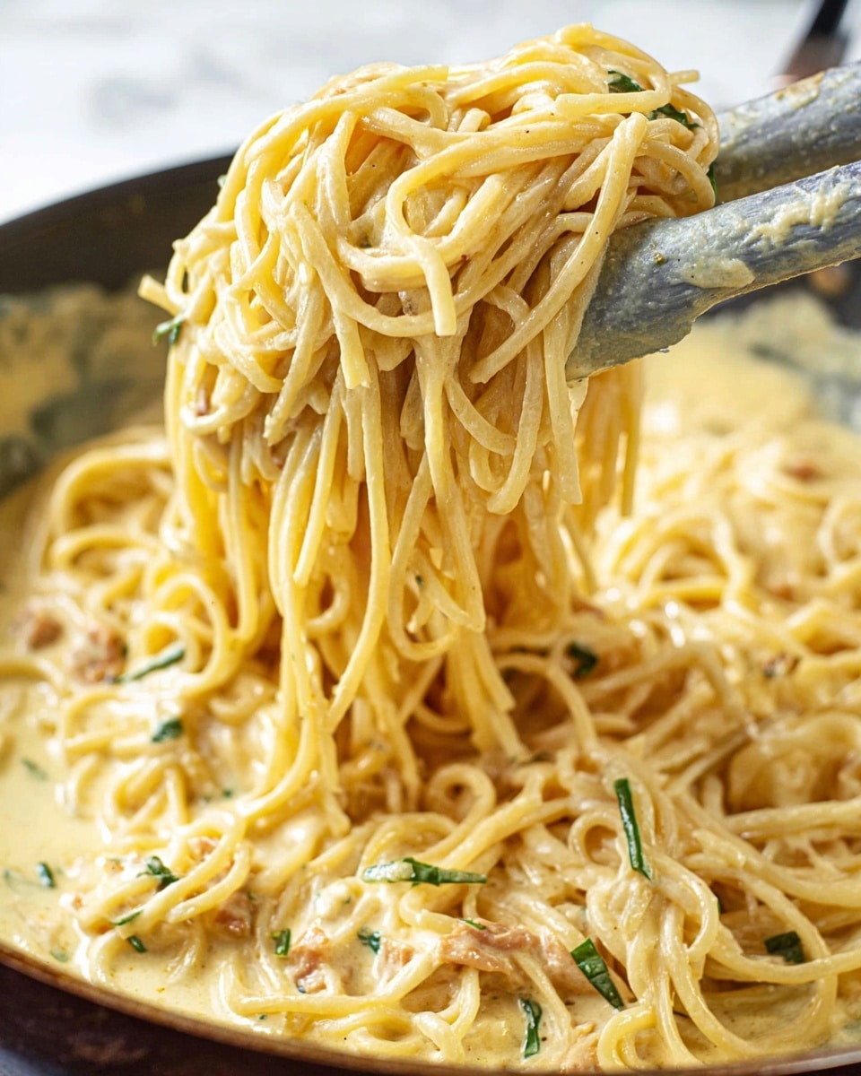 A close-up of creamy pasta being lifted with a spatula from a pan, showing long yellowish spaghetti noodles mixed in a thick pale yellow sauce with small pieces of light brown bits and thin strips of green herbs, the sauce coating the noodles smoothly, set against a white marbled background. photo taken with an iphone --ar 4:5 --v 7