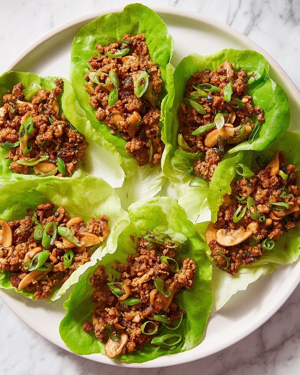 A white round plate holds six lettuce wraps arranged in a circle. Each wrap uses a bright green lettuce leaf as the base, holding a layer of cooked ground meat mixed with small pieces of light brown mushrooms and cooked onions. The meat mixture is a rich brown color, showing a slightly textured surface with small bits of herbs and spices. The wraps are topped with thin slices of fresh, green spring onion rings scattered evenly over the meat. The plate rests on a white marbled surface, adding a clean, elegant backdrop. photo taken with an iphone --ar 4:5 --v 7