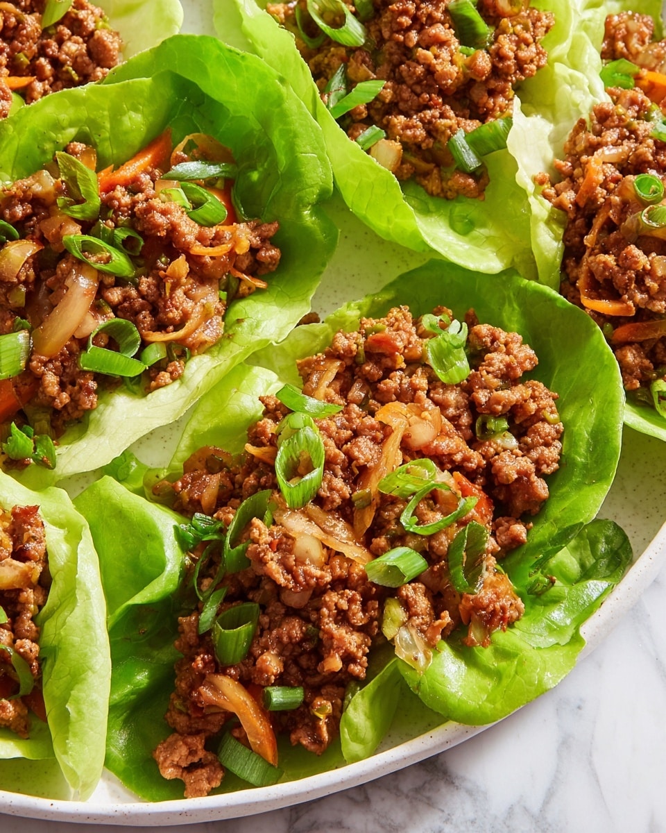 The image shows several green lettuce cups filled with a mix of cooked ground meat and sliced vegetables. The filling is brown and textured, with visible pieces of lightly cooked onions and thin slices of orange carrots. Bright green chopped scallions are sprinkled on top of each lettuce cup, adding freshness. The lettuce cups are arranged closely together on a white plate, which sits on a white marbled surface. The colors range from the bright green of the lettuce and scallions to the warm brown and orange tones of the cooked filling. photo taken with an iphone --ar 4:5 --v 7