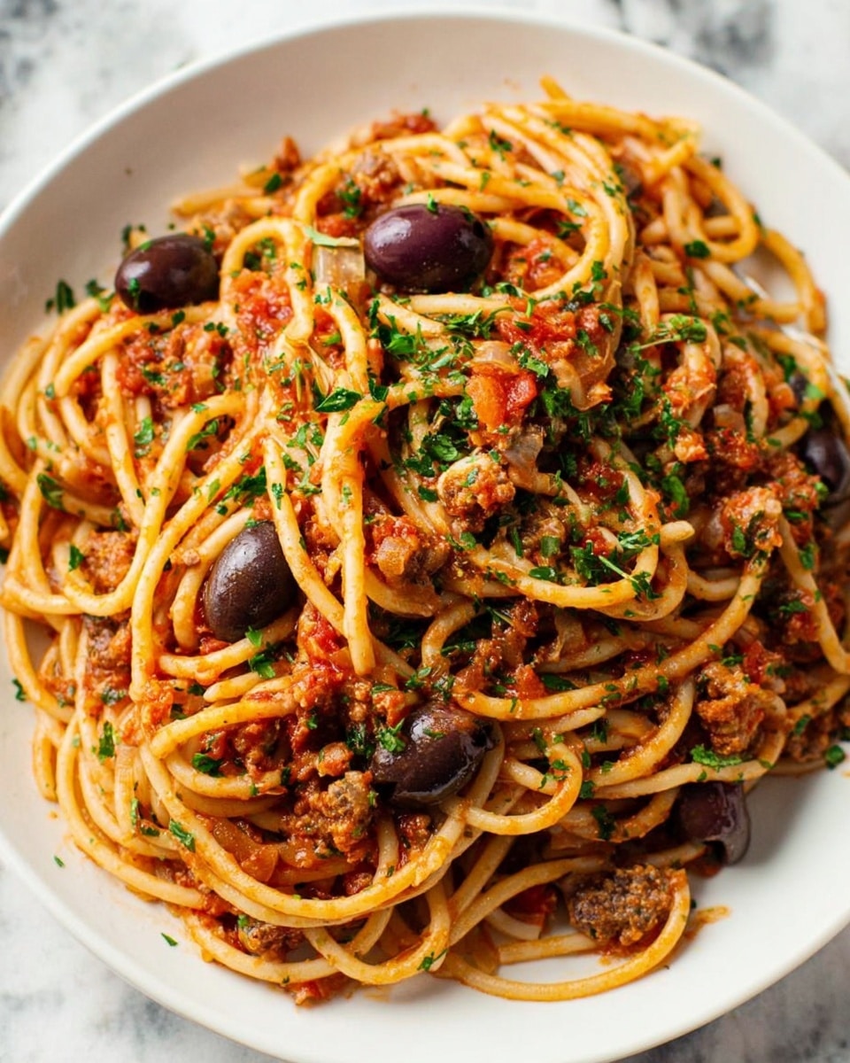 A white plate filled with spaghetti pasta mixed with a red tomato sauce, garnished with chopped green herbs. The pasta strands are thick and intertwined, coated evenly with the sauce. Dark brown olives and small chunks of meat are scattered throughout the dish, adding texture and depth. The plate sits on a white marbled surface, creating a clean, fresh look. The overall presentation is warm and inviting, with a rustic, homemade feel. Photo taken with an iphone --ar 4:5 --v 7