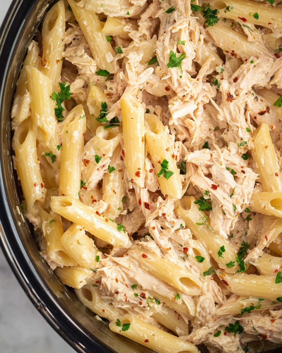 A close-up shows a big spoon lifting creamy pasta mixed with shredded chicken from a black pot. The pasta is penne, yellowish and smooth, covered with thick creamy sauce mixed with small red chili bits and herbs. The shredded chicken pieces are soft and blend well with the sauce. The pot’s inside is dark, and the creamy pasta fills most of the pot's space. The background is a white marbled texture. photo taken with an iphone --ar 4:5 --v 7