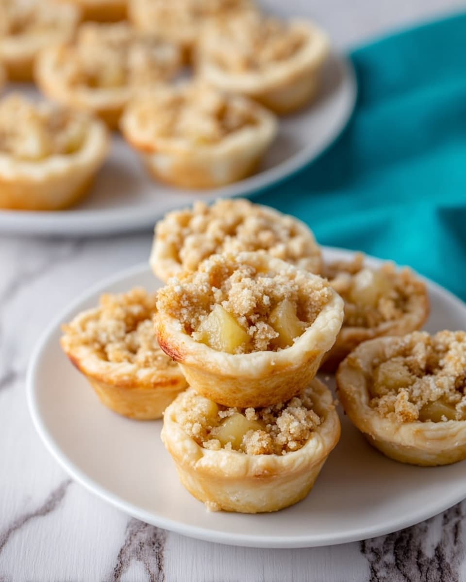 The image shows a blue plate filled with eight small tarts. Each tart has two layers: the bottom layer is a golden, flaky crust that holds the shape of the tart, and the top layer is a crumbly, white topping that looks soft and slightly powdery. The tarts are arranged closely together on the plate, which sits on a white marbled surface. In the background, there is a dark baking tray with more tarts visible, some with the same crumbly white top. Photo taken with an iphone --ar 4:5 --v 7