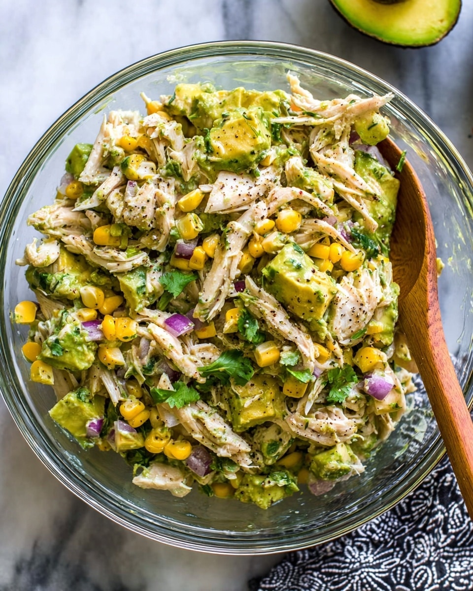 A clear glass bowl holds a colorful mixed salad on a white marbled surface. The salad has five main layers: shredded light beige chicken on the left, bright green avocado chunks with a creamy texture on the top right, a small bunch of chopped green herbs at the top left, yellow corn kernels slightly shiny and piled on the middle right, and finely chopped purple-red onion pieces at the bottom right. Black pepper is sprinkled on all ingredients, adding contrast. Another image shows the salad mixed, with all ingredients combined, revealing a creamy, slightly chunky texture with the colorful pieces spread evenly. A metal and wooden spoon are placed inside the bowl, with half an avocado in the background. Photo taken with an iphone --ar 4:5 --v 7