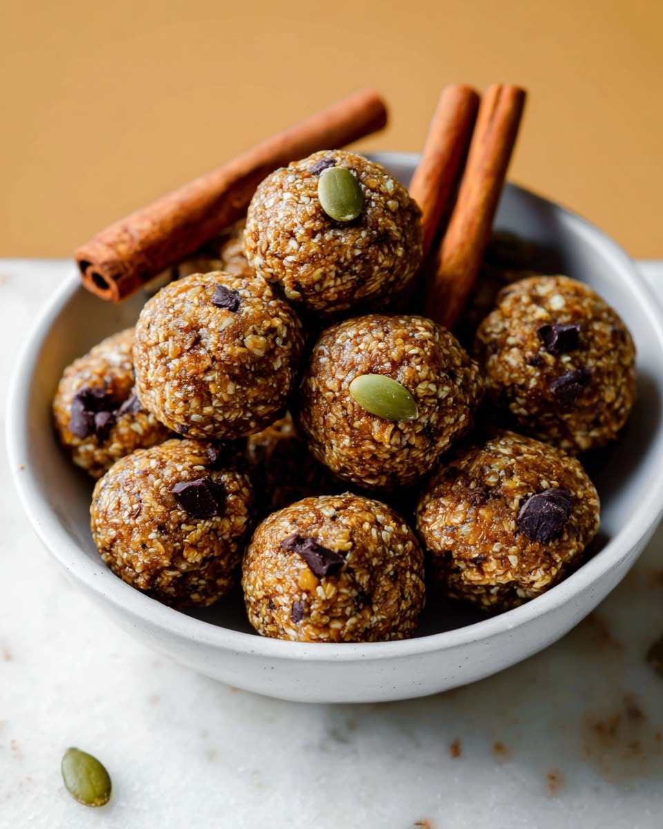 The image shows several round energy balls made from oats, seeds, and small dark bits like chocolate chips or dried fruit, all mixed into a dense, textured golden-brown base. There is one energy ball in the center topped with a single green pumpkin seed. Three cinnamon sticks of reddish-brown color lay on top, resting among the energy balls. The background has a soft focus but reveals a white marbled surface. photo taken with an iphone --ar 4:5 --v 7