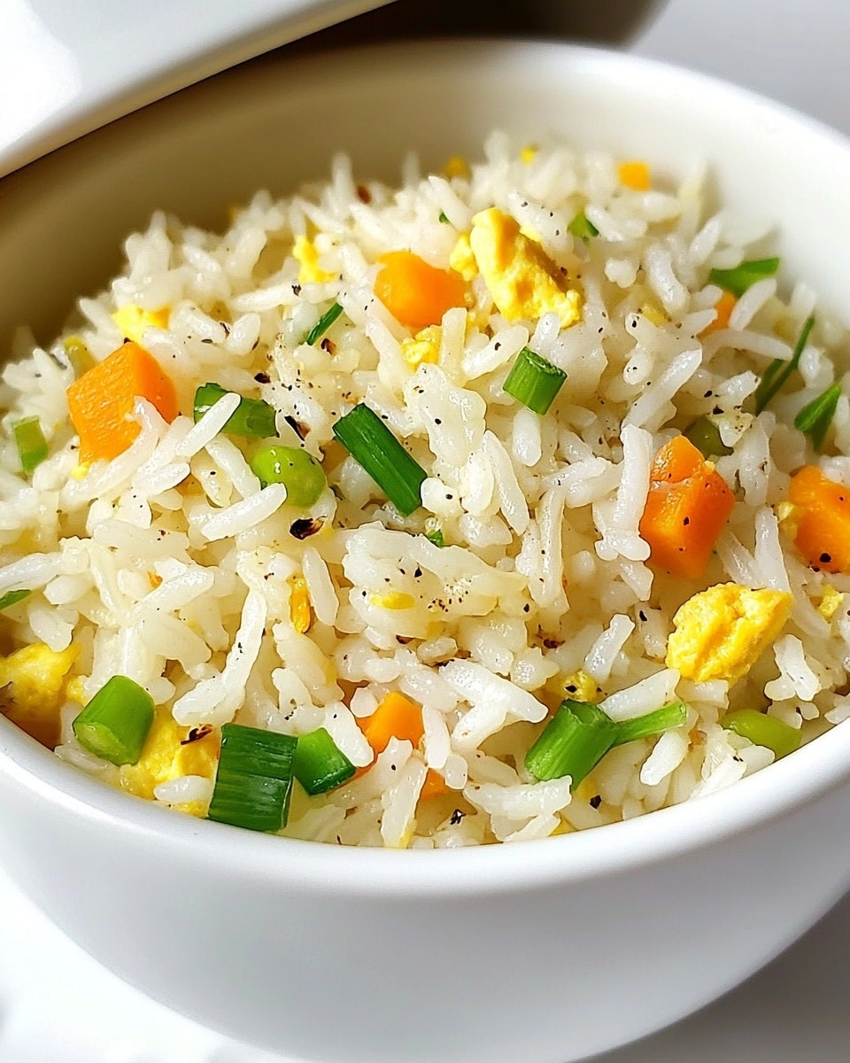 The image shows a close-up of cooked white rice with finely chopped green onions, small orange carrot cubes, and bits of yellow egg mixed evenly throughout. The rice has a light texture with slight black pepper specks, adding contrast. All this is served inside a white bowl with a matching white lid placed behind it. The background is a white marbled surface. photo taken with an iphone --ar 4:5 --v 6.1