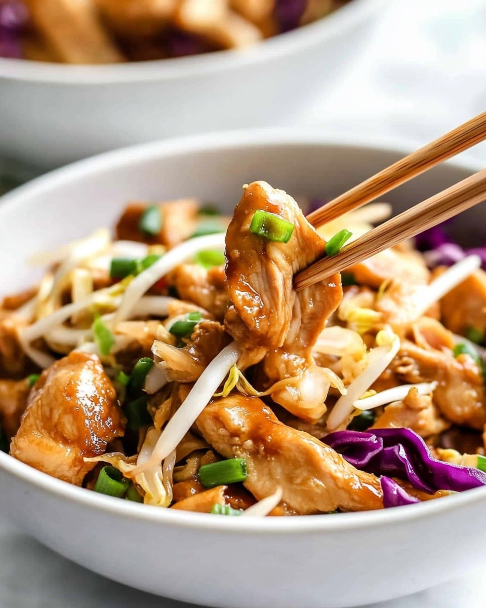 A close-up of a white bowl filled with stir-fried chicken pieces mixed with shredded cabbage, bean sprouts, and chopped green onions. The chicken pieces are golden brown and glossy, layered with light beige bean sprouts, vibrant green onions, and bits of purple cabbage. A pair of wooden chopsticks held by a woman's hand picks up a portion of the chicken and cabbage mix, with a piece of purple cabbage visible in the middle. The bowl sits on a white marbled surface, with another bowl blurred in the background. photo taken with an iphone --ar 4:5 --v 6.1