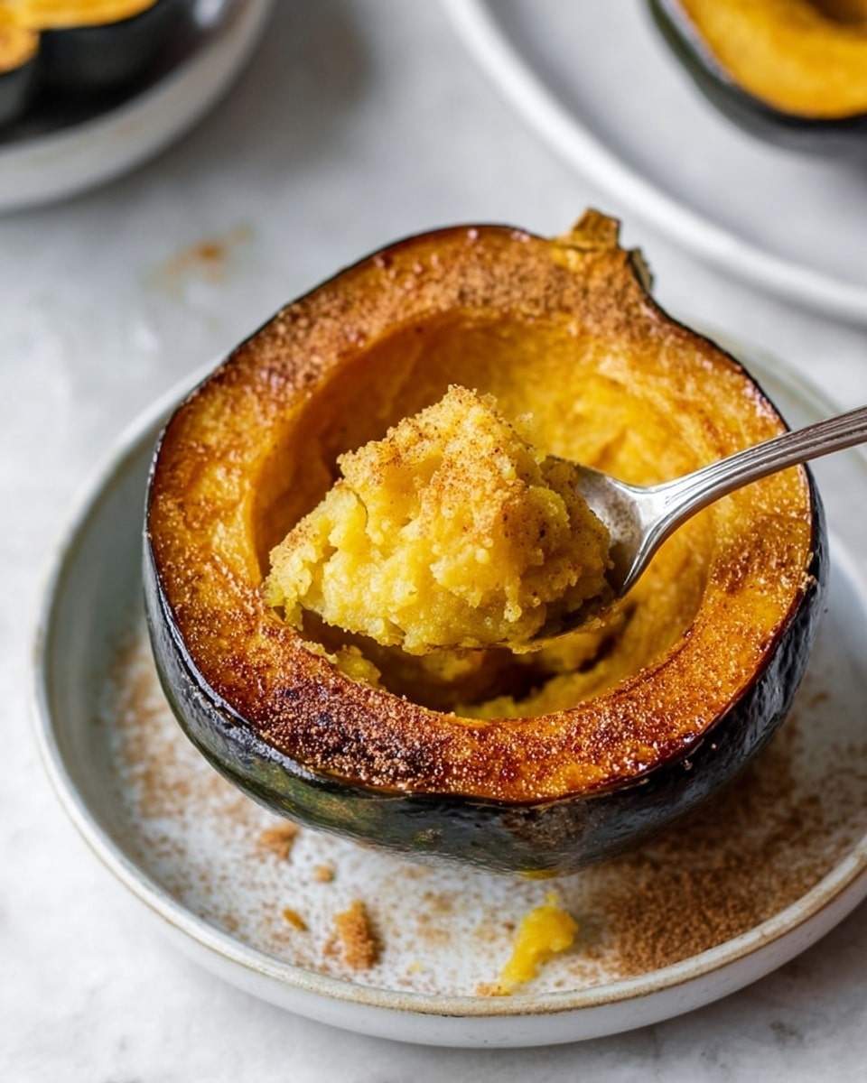 A roasted acorn squash half is shown on a white plate with a white marbled surface underneath. The squash skin is dark green and textured, with the inside bright yellow-orange and soft. The edges of the squash are dusted with a light brown spice, giving it a slightly rough look. A silver spoon is scooping a soft, mashed portion from the hollow center of the squash. Crumbs and small spice spots are scattered around the plate. Photo taken with an iphone --ar 4:5 --v 7
