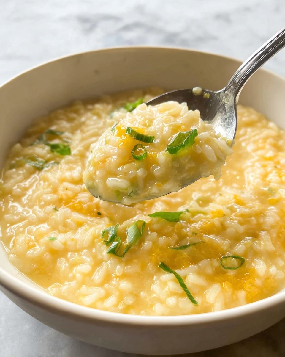 A brown bowl filled with a creamy soup that has a soft, slightly lumpy texture in a light yellow color, topped with bright green chopped scallions clustered in the center. The bowl sits on a cloth with gray and blue stripes, next to a silver spoon with a smooth, rounded shape. In the background, a larger white bowl with a textured surface holds more of the same soup, all placed on a white marbled surface. photo taken with an iphone --ar 4:5 --v 7