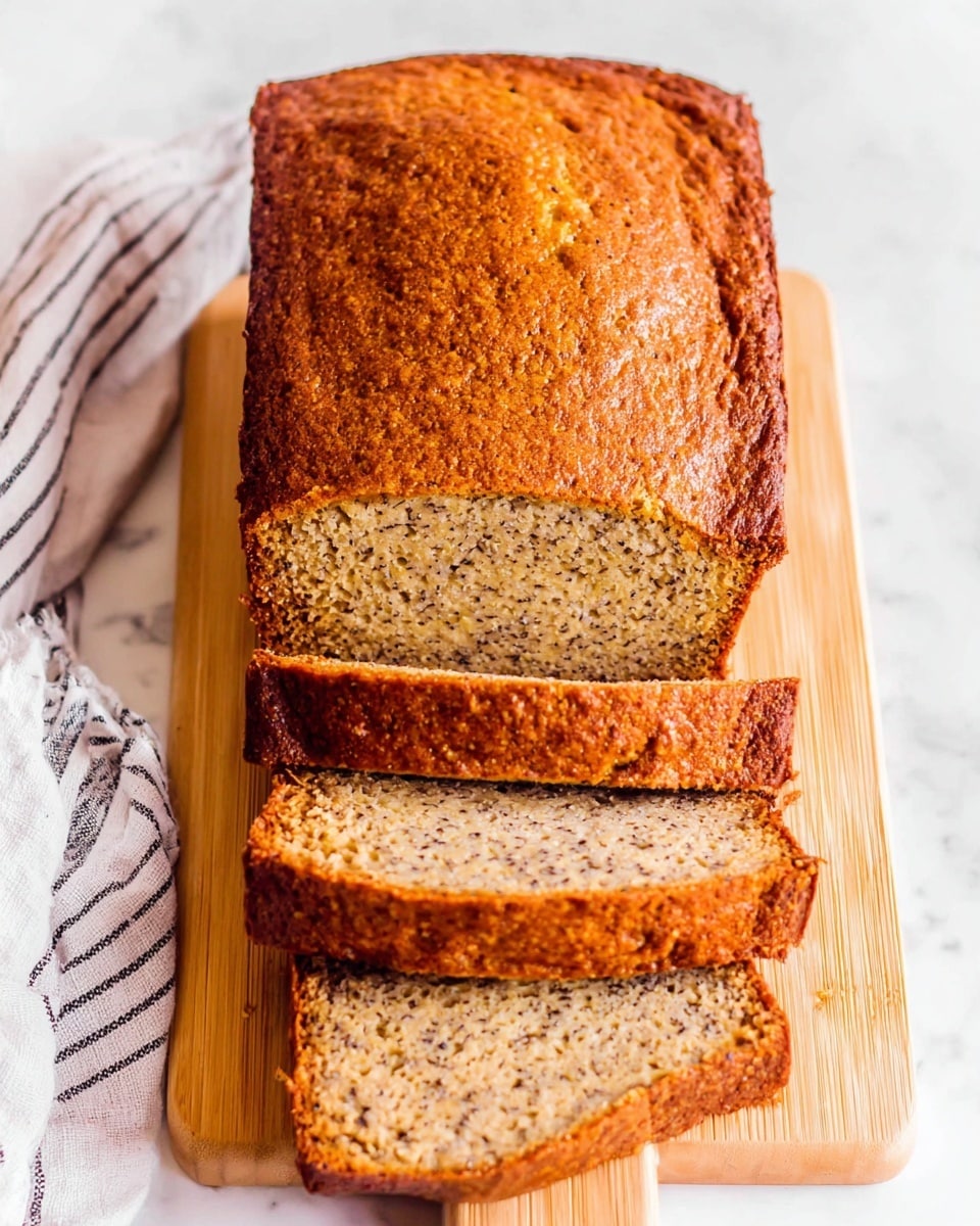 The image shows a close-up of a single thick slice of banana bread with a golden-brown crust and a light tan inside speckled with small darker bits, all placed on a light wooden cutting board set on a white marbled surface. The texture of the bread is soft and moist with small air pockets spread evenly throughout. The top crust has a slightly rough and uneven look with some baked cracks and darker spots around the edges. Photo taken with an iphone --ar 4:5 --v 7