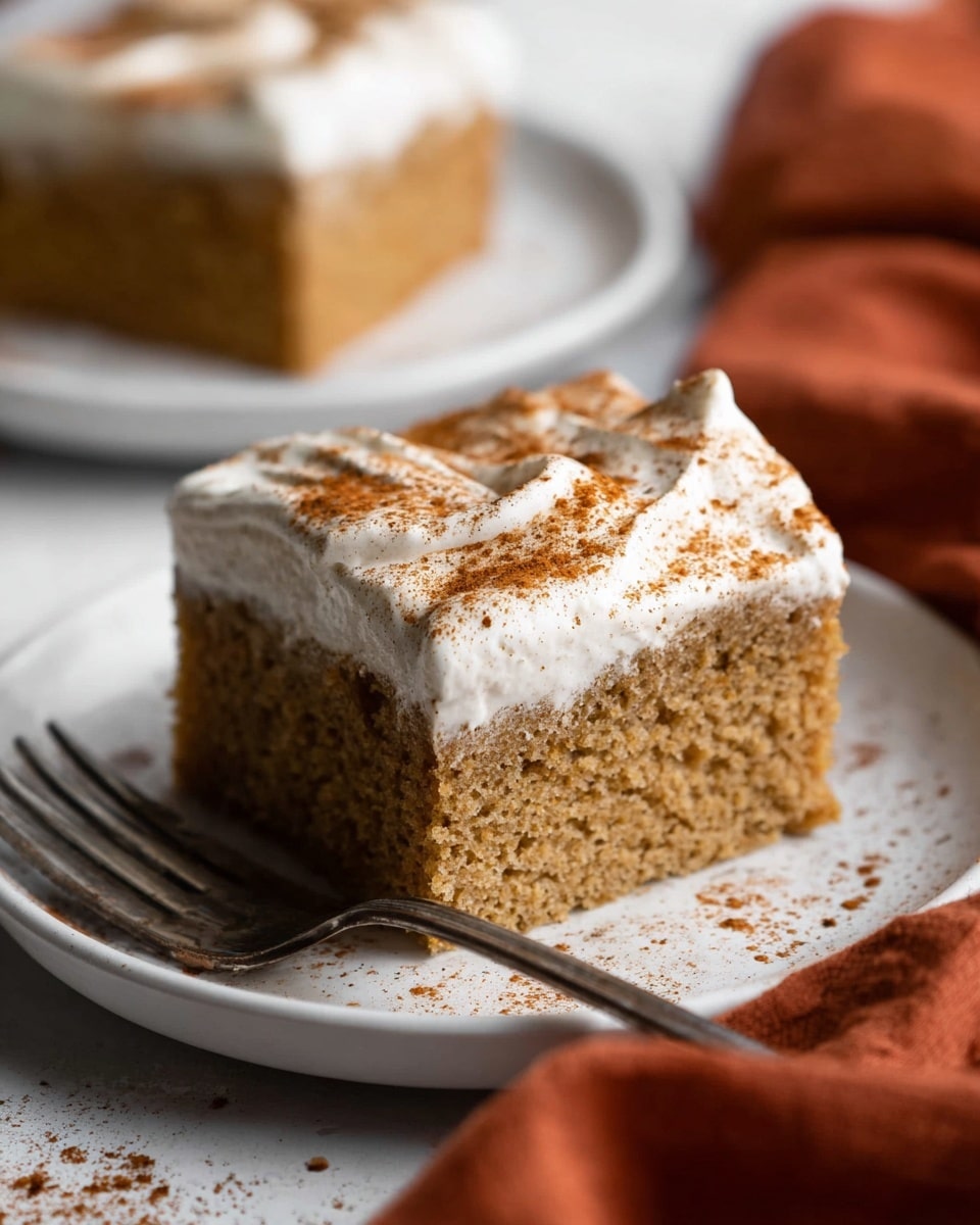 A single square piece of light brown cake sits on a white plate with a slightly raised edge on a white marbled surface. The cake has a fluffy texture with small air holes visible, and it is topped with a thick layer of white frosting that is smooth and spread evenly. The frosting is sprinkled with a fine layer of brown powder, likely cinnamon, mostly concentrated on the right side. There is a bit of light yellow liquid around the base of the cake on the plate. A silver fork rests on the edge of the plate, and a burnt orange cloth is partially visible at the bottom left corner. In the background, there is a clear plastic egg carton with a label that is slightly blurred. Photo taken with an iphone --ar 4:5 --v 7