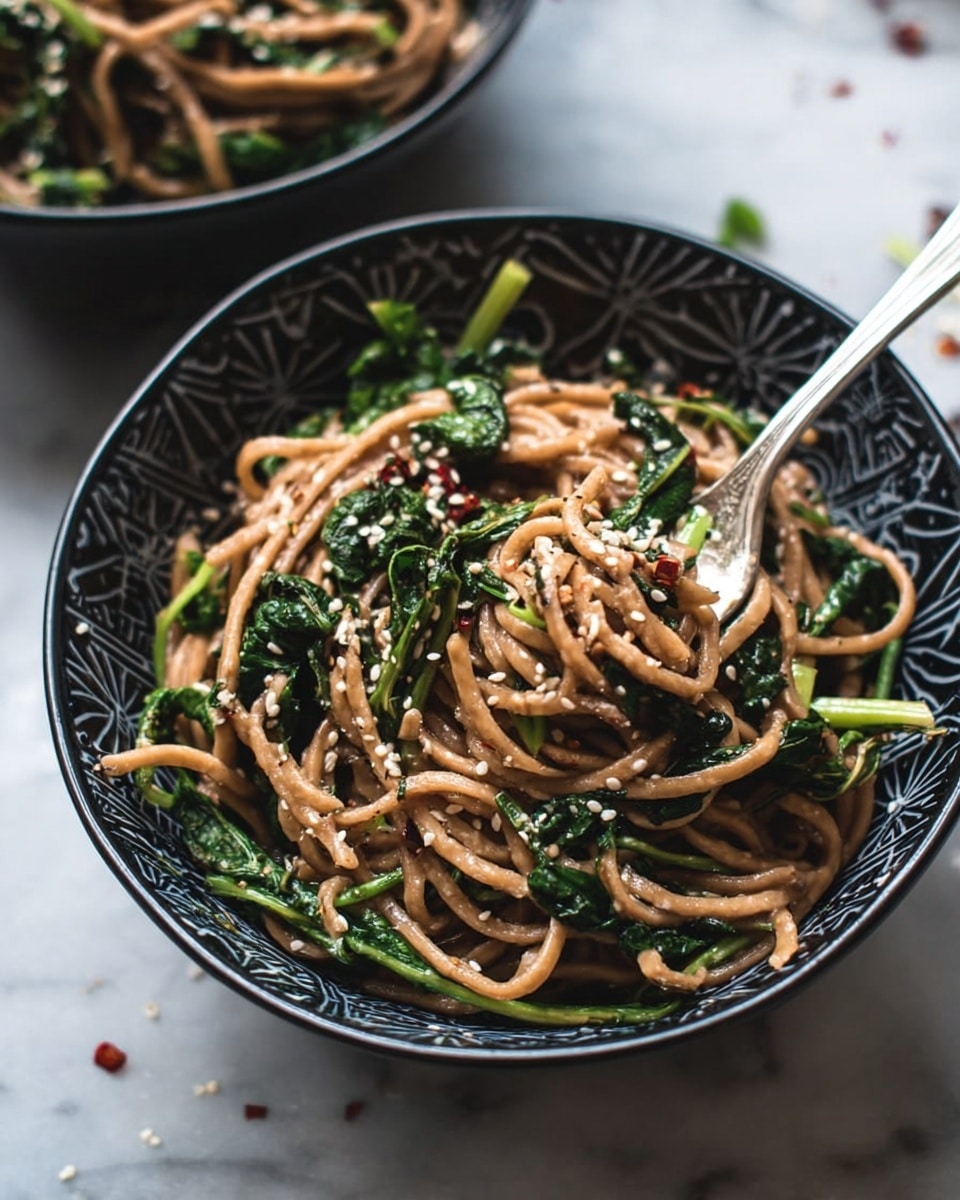 A shiny silver fork lies on a white marbled surface, with a small tangle of light brown noodles wrapped around its prongs. Mixed within the noodles are bright green pieces of asparagus with a slightly glossy texture, giving a fresh look. Small bits of white sesame seeds and tiny red pepper flakes are scattered around the fork on the surface. The background is soft and blurred, focusing attention on the fork and the food wrapped around it. photo taken with an iphone --ar 4:5 --v 7