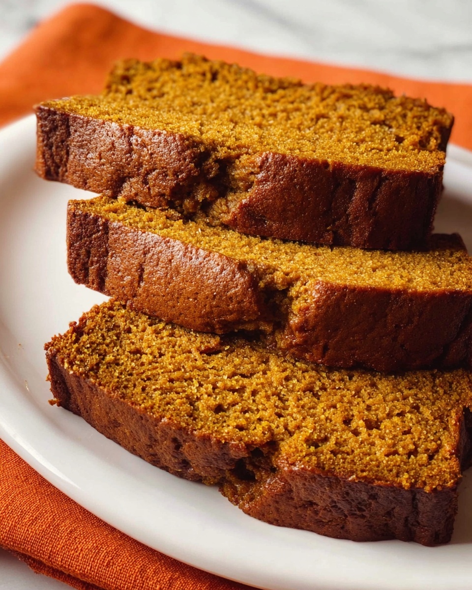 Three slices of moist pumpkin bread with a warm brown color and slightly rough texture are stacked on a white plate. The top crust is darker and has a slightly uneven, cracked surface, while the inside is soft and dense. The plate is placed on a white marbled surface with an orange cloth partially visible under it. Photo taken with an iphone --ar 4:5 --v 7