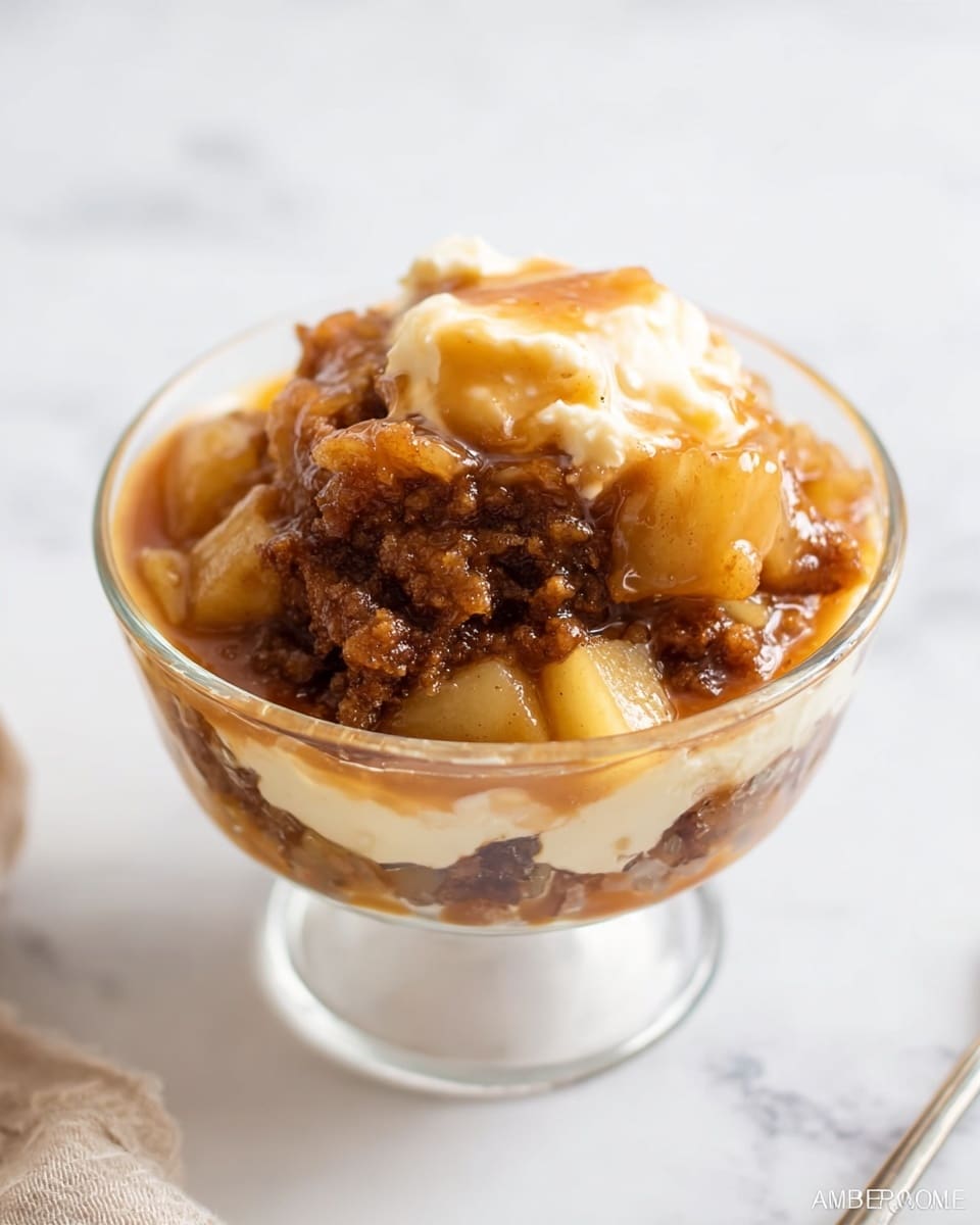 A clear glass bowl on a white marbled surface holds a warm dessert with about three layers. The bottom layer has soft, light yellow apple pieces, some with a smooth texture. Above that is a thick, brown, crumbly cake layer that looks moist and dense. The top layer is covered with a shiny, golden-brown sauce that is smooth and syrupy, lightly flowing around the cake and apples. A soft cream or butter piece is melting on top, adding a light yellow contrast to the sauce. Photo taken with an iphone --ar 4:5 --v 7