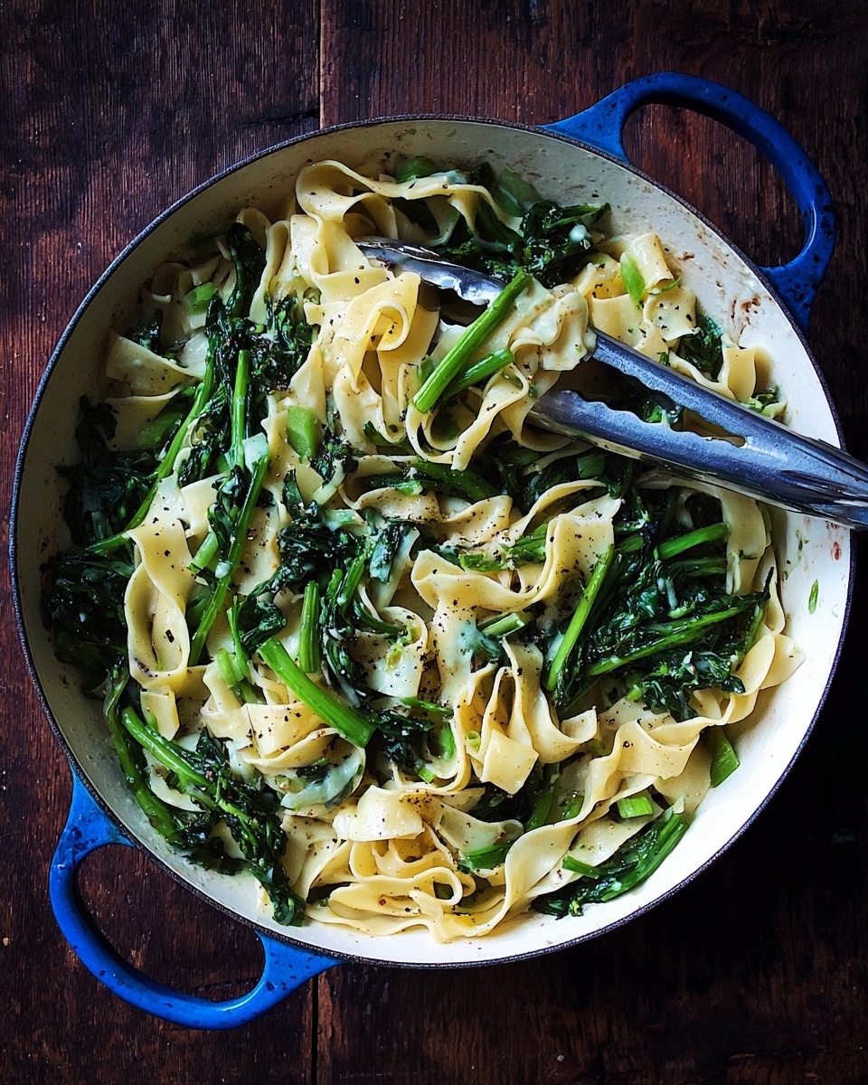 The image shows a white plate filled with wide, flat pasta noodles, lightly coated in a creamy sauce. Mixed throughout the noodles are several pieces of dark green leafy vegetables, slightly wilted but still vibrant with some stems visible. The dish is sprinkled with a generous amount of black pepper, adding small dark specks over the noodles and greens. A silver fork rests on the edge of the plate, partially inserted into the pasta, on a white marbled surface. photo taken with an iphone --ar 4:5 --v 7