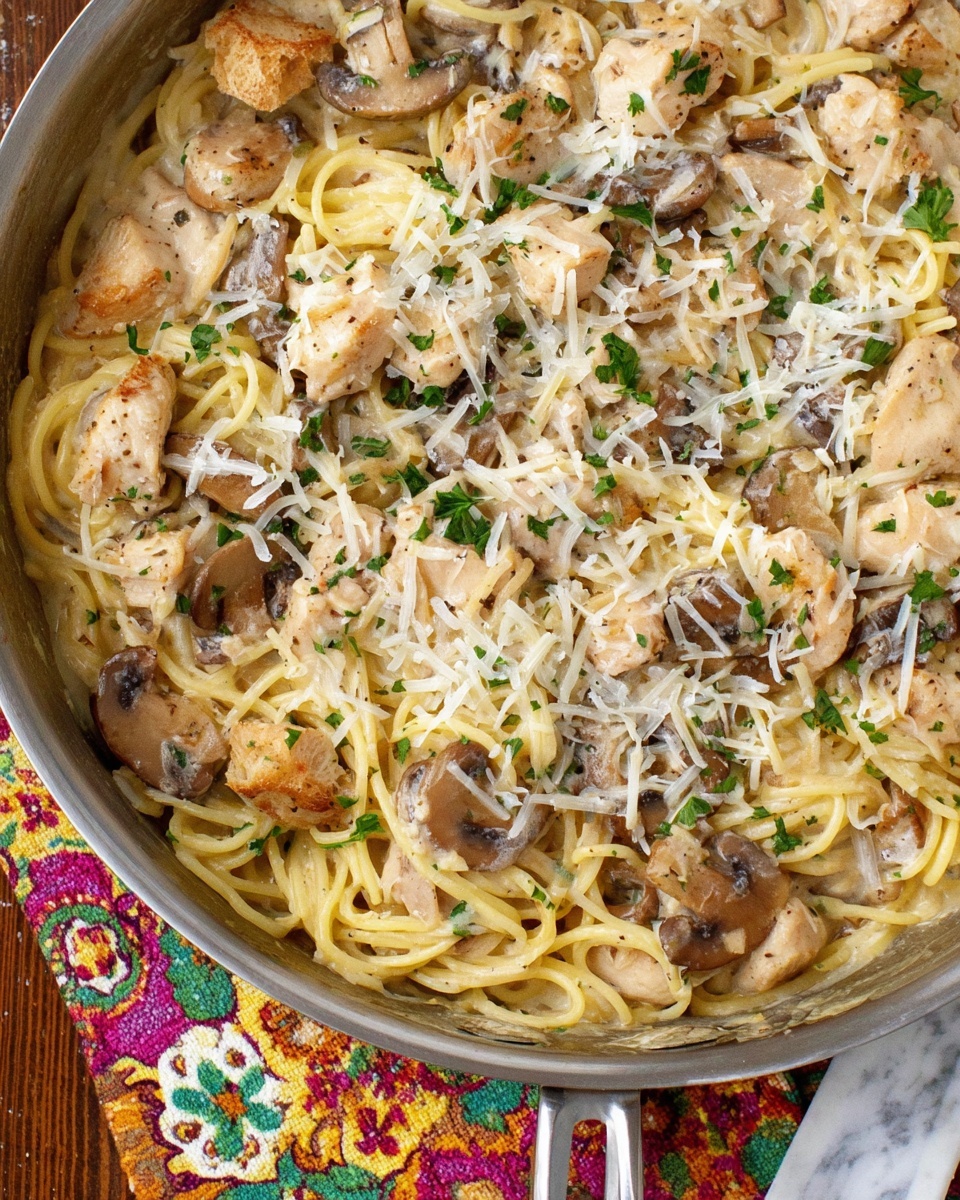A white plate holds a serving of spaghetti pasta with three main layers: smooth, pale cream sauce coated noodles form the base, mixed with chunky pieces of light beige chicken scattered evenly, and dark brown sliced mushrooms placed throughout. Small green herbs are sprinkled on top for color, along with thin shreds of white cheese. A silver fork with a wooden handle rests on the right side, its prongs partly buried in the noodles. The plate sits on a rustic wooden surface with a colorful floral cloth nearby. Photo taken with an iphone --ar 4:5 --v 7