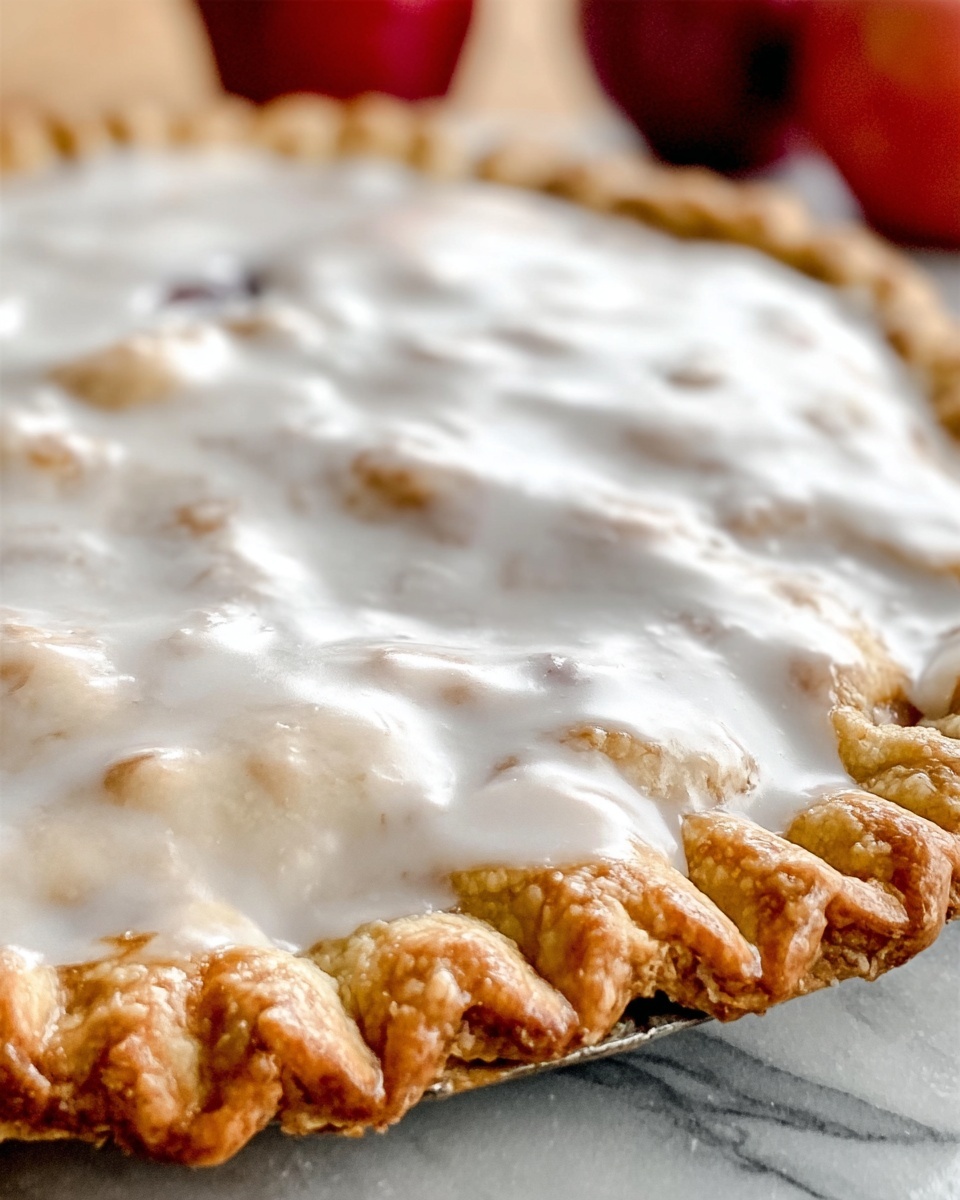 The image shows a close-up of a single-layer pie with a golden, flaky crust that has a detailed crimped edge. The filling is covered by a smooth, glossy white icing layer that looks slightly thick and evenly spread across the top. The pie sits on a white marbled surface with a few red apples blurred in the background, adding a pop of color. Photo taken with an iphone --ar 4:5 --v 7