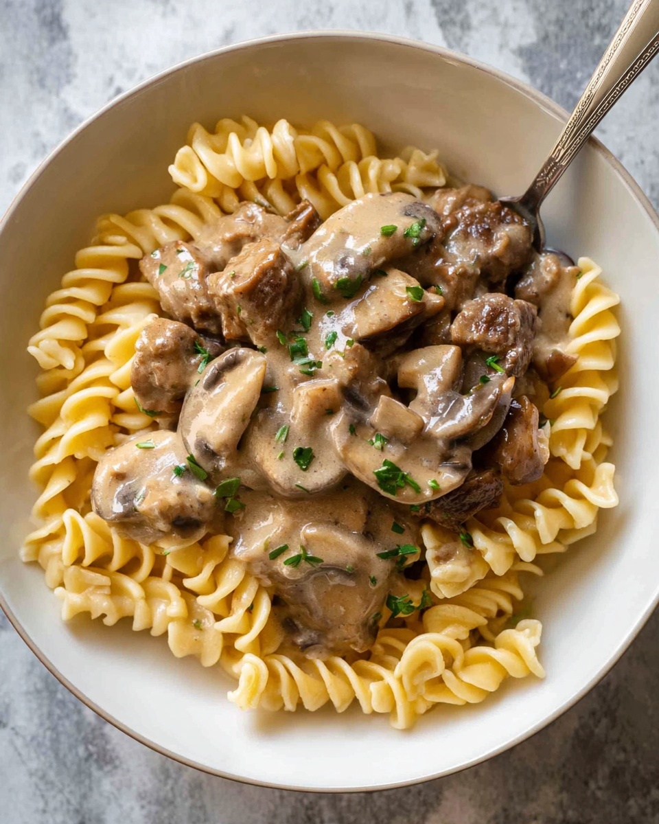 A close-up view of a black pan filled with a creamy, light brown sauce that has several pieces of cooked brown meat and sliced mushrooms mixed throughout. The sauce looks smooth and thick, with small green herbs sprinkled on top for color. A silver spoon is partly dipped into the sauce, showing the creamy texture and some of the ingredients. The pan sits on a white marbled surface. photo taken with an iphone --ar 4:5 --v 7