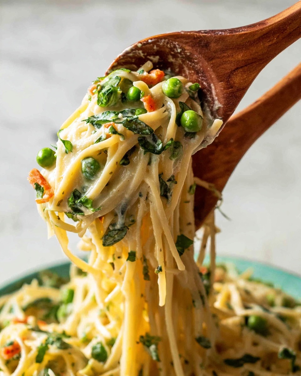 A white bowl holds a creamy pasta dish with about four layers visible. The bottom layer shows thick yellow noodles, loosely coiled. On top are slices of light green zucchini and dark brown mushrooms scattered around. Bright green peas and snap peas add color, mixed with small red cherry tomato halves. A layer of creamy sauce covers parts of the pasta and vegetables, giving a smooth texture. The dish is sprinkled with light brown pine nuts and white grated cheese. A silver fork with tomato on it rests on the right side of the bowl. The bowl sits on a white marbled surface with a black and white striped cloth nearby. Photo taken with an iphone --ar 4:5 --v 7