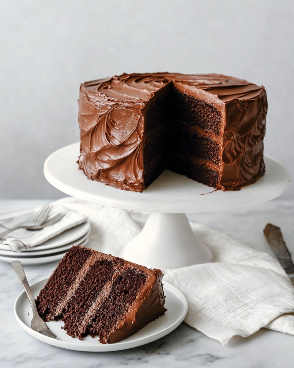 A three-layer chocolate cake is shown, each layer dark brown with a moist texture. The cake is covered all over with thick, shiny, and smooth chocolate frosting that is swirled to create textured patterns on the sides and top. A large slice is missing from the cake, revealing the dark inside and frosting between the layers. A slice of the cake is placed on a small white plate in front, showing the three distinct chocolate layers with frosting in between and on the outside edges. The plate sits on a white marbled surface beside a silver fork and a white cloth napkin. The whole cake is displayed on a white cake stand with a pedestal base. The background is neutral and simple. photo taken with an iphone --ar 4:5 --v 7