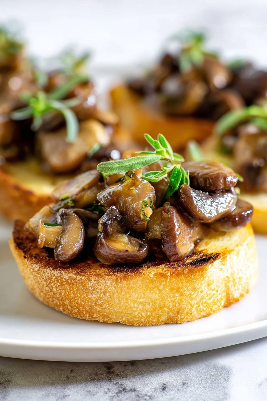 The image shows a close-up of a small round toast slice as the base, golden brown with light grill marks and a slightly rough texture. On top of the toast is a generous layer of sautéed mushrooms in varying shades of brown, some shiny from oil, with a mix of small and large mushroom pieces creating a textured and chunky look. The mushrooms are garnished with small fresh green herb sprigs placed on top, adding a pop of color. The toast with mushrooms is placed on a white plate set against a white marbled background. photo taken with an iphone --ar 2:3 --v 7 - Mushroom Thyme Crostini, Mushroom Crostini appetizer, Easy mushroom crostini, Gourmet mushroom crostini, Toasted bread with mushrooms