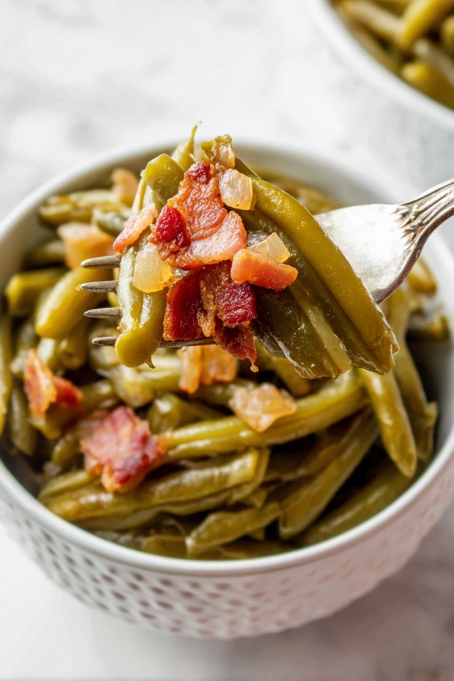 A white bowl with a pattern holds cooked green beans layered at the bottom, soft and shiny with a slightly wrinkled texture. On top, small chunky pieces of browned bacon with a reddish-brown tone and a bit of translucent cooked onion are mixed in. A fork lifts some green beans and bacon from the bowl, showing the layers clearly, with the vegetables still moist and the bacon crispy in places. The background is a white marbled surface. photo taken with an iphone --ar 2:3 --v 7 - Crock Pot Green Beans with Bacon, green beans with bacon, slow cooker green beans, bacon side dish, flavorful green bean recipe