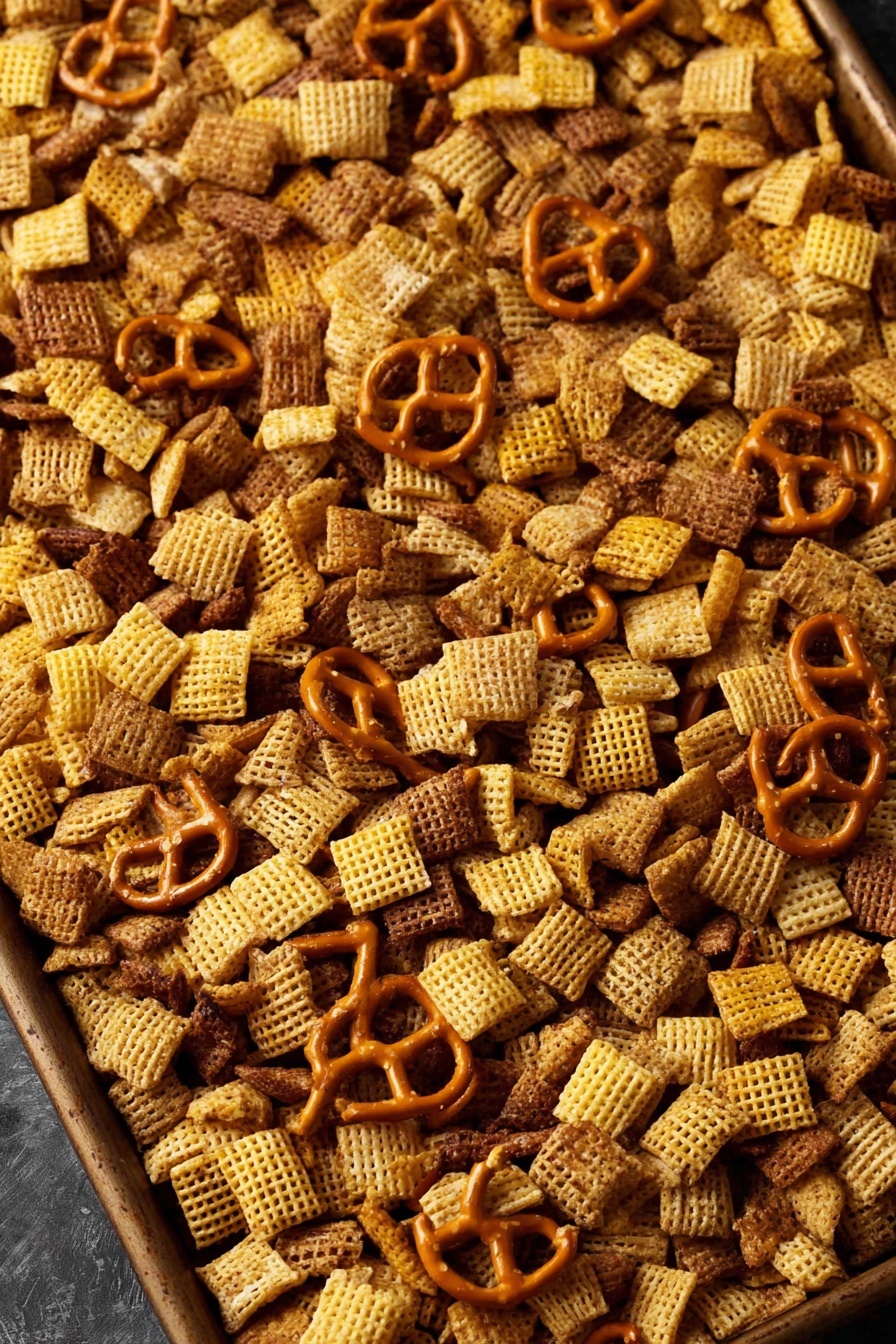 A large baking tray filled with a snack mix that has three main layers: light yellow square cereal pieces with a woven texture, small golden-brown pretzel shapes scattered across, and thin, rounded brown cracker pieces evenly mixed throughout. The snack mix layers blend together with a crunchy texture, sitting on a dark surface. The colors range from light yellow to brown and golden orange, creating a warm and inviting look. Photo taken with an iphone --ar 2:3 --v 7 - Homemade Chex Mix, savory snack mix, crunchy party snacks, DIY Chex Mix, easy snack recipes