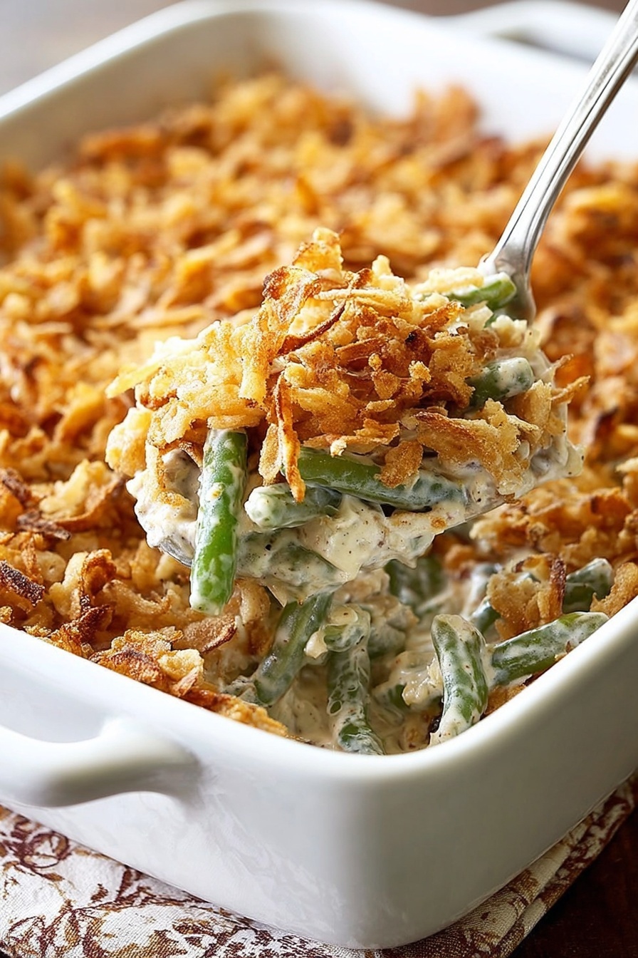 A white rectangular baking dish filled with a creamy green bean casserole topped with a thick layer of crispy golden brown fried onions. The casserole shows soft green beans mixed with a light beige creamy sauce beneath the crunchy topping. In the foreground, a white spoon lifts a serving, revealing the creamy texture mixed with green beans and bits of fried onions. The dish is placed on a table with a white marbled texture showing under the edges. Photo taken with an iphone --ar 2:3 --v 7 - Green Bean Casserole with Bacon and Mushrooms, Green Bean Casserole recipe, Bacon and Mushroom Green Bean Side Dish, Holiday Green Bean Casserole, Easy Green Bean Casserole