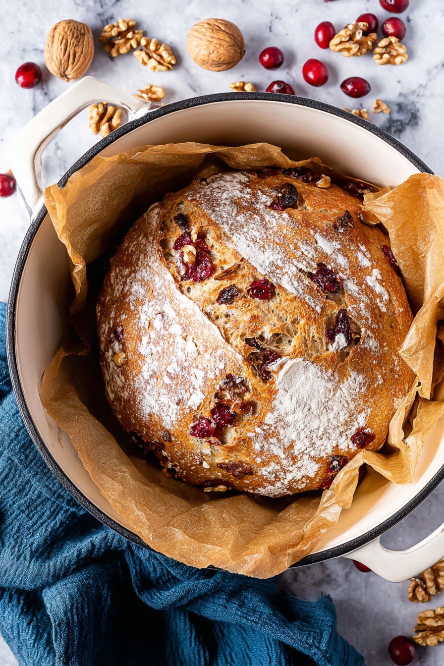 A close-up image shows two thick slices of bread placed on a wooden board against a white marbled texture background. The bread has a golden-brown crust and a light beige inside filled with visible pieces of red cranberries and light brown walnuts spread evenly throughout. The texture looks soft with small holes in the crumb. In the top left corner of the image, there are some walnut pieces and dried cranberries scattered on the wooden board. A dark gray cloth is also partly visible in the upper right area. photo taken with an iphone --ar 2:3 --v 7 - No-Knead Cranberry Walnut Bread, easy cranberry walnut bread, rustic holiday bread, no-knead bread recipes, festive cranberry walnut loaf