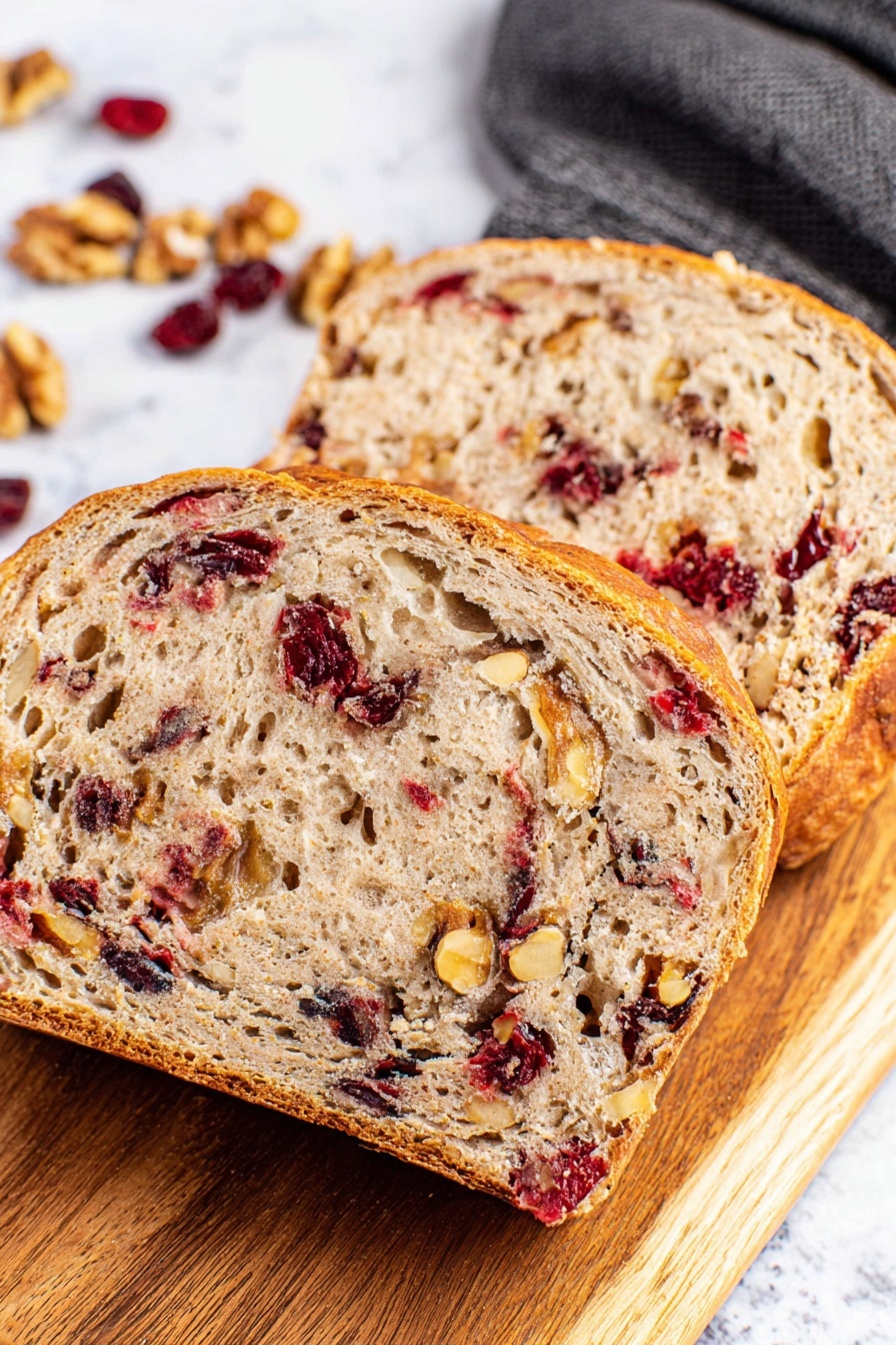 A round loaf of bread with a golden brown crust dusted with white flour is placed in a white pot lined with parchment paper. Visible inside the crust are pieces of red cranberries and light brown walnuts, adding texture and color contrast. Around the pot on the white marbled surface, whole walnuts and scattered dried cranberries create a natural decoration. A dark blue cloth rests partially under the pot’s handle, adding a soft touch to the scene. The overall look shows a rustic, fresh bread with a mix of crunchy and chewy textures photo taken with an iphone --ar 2:3 --v 7 - No-Knead Cranberry Walnut Bread, easy cranberry walnut bread, rustic holiday bread, no-knead bread recipes, festive cranberry walnut loaf