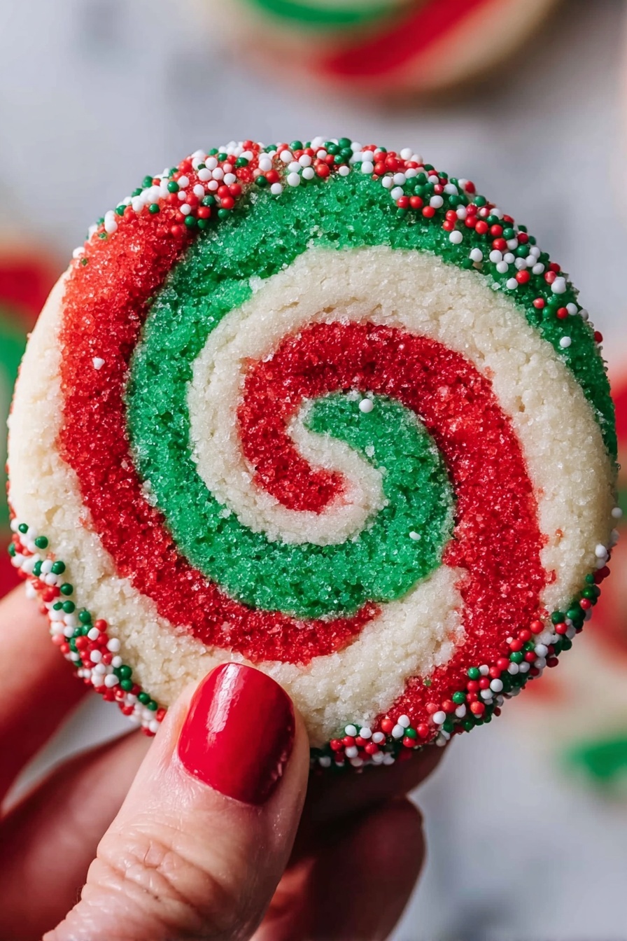 A round cookie with a red, white, and green swirl pattern that forms a spiral from the center to the edges. The outer edge of the cookie is coated with small red, white, and green round sprinkles. A woman's hand with red nail polish holds the cookie against a blurred background, and the surface under the cookie is white marbled texture. photo taken with an iphone --ar 2:3 --v 7 - Swirled Christmas Cookies, festive holiday cookies, Christmas cookie recipes, colorful holiday cookies, easy Christmas treats