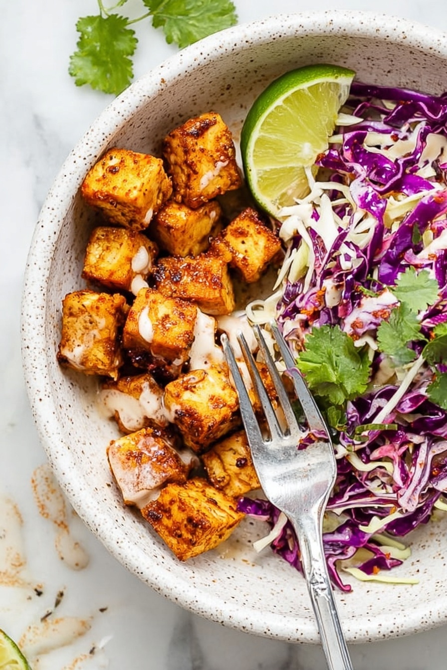 The image shows a white speckled bowl with two main layers: on one side, there are small, golden-brown seasoned cubes with a smooth light sauce drizzled over them, and on the other side, there is a mix of shredded purple and white cabbage with some green cilantro leaves scattered on top. A wedge of bright green lime sits at the edge of the bowl. A silver fork is placed inside, resting on the bowl’s edge and touching some of the cubes. The bowl is on a white marbled surface with some sauce drops visible nearby. Photo taken with an iphone --ar 2:3 --v 7 - Spicy Fish Taco Bowl, Fish Taco Bowl, Spicy Fish Bowl, Easy Fish Taco Dinner, Quick Fish Taco Recipe
