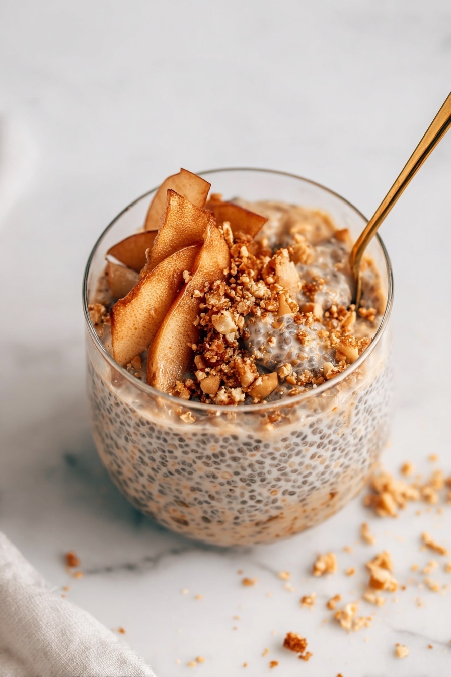A clear glass filled with three main layers is shown on a white marbled surface. The bottom layer is a thick, creamy mixture with visible small black chia seeds evenly distributed, giving it a speckled texture. On top of that, there is a layer of thin, light brown apple slices with a soft texture, slightly curled and overlapping in a loose arrangement. The top layer is sprinkled with small, coarse granules of golden brown crumbs and chopped nuts, adding a crunchy texture and contrasting color. A gold spoon is inserted on the right side of the glass, partly immersed in the layers. Some crumbs are scattered around on the white marbled surface near the glass, showing slight messiness. photo taken with an iphone --ar 2:3 --v 7 - Apple Cinnamon Chia Pudding with Stewed Apples, healthy chia pudding recipes, cozy breakfast ideas, easy fruit dessert, vegan apple pudding