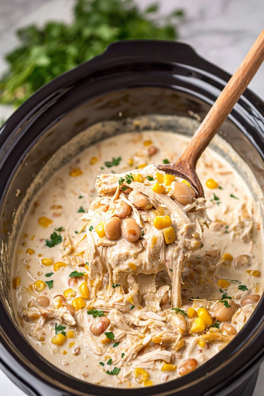 The image shows a close-up of a creamy stew inside a black slow cooker. The stew has three main layers: a base of creamy beige sauce with a smooth texture, shredded white chicken pieces scattered throughout, and mixed beans of light brown and reddish colors along with yellow corn kernels evenly spread. Some small bits of green herbs are sprinkled on top for a touch of color. A wooden spoon lifts a portion of the stew, showing all the layers clearly in the spoon's bowl. The background features a bunch of fresh green herbs slightly blurred, and the scene is set on a white marbled surface. Photo taken with an iphone --ar 2:3 --v 7 - Creamy Crockpot White Chicken Chili, slow cooker white chicken chili, easy white chicken chili recipe, comforting chicken chili, creamy chicken chili Crockpot