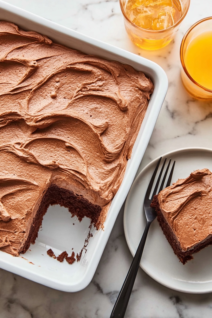 A white rectangular baking dish holds a thick layer of smooth, light brown chocolate frosting spread evenly, with visible swirls and soft peaks on top. One square piece has been removed from the bottom right corner of the dish, showing a dark brown chocolate cake layer beneath the frosting. Next to the dish, on a small white round plate, sits the removed cake piece with the same rich frosting on top, accompanied by a black fork resting beside it. In the top right corner, there is a glass of orange drink on the white marbled surface. Photo taken with an iphone --ar 2:3 --v 7 - Chocolate Mayonnaise Sheet Cake, chocolate mayonnaise cake, moist chocolate cake, simple sheet cake recipe, easy chocolate cake