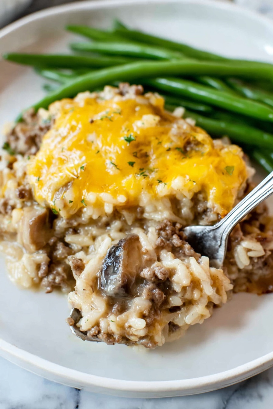 The dish shows two main layers on a white plate with green beans at the back. The bottom layer is a mix of cooked rice, ground meat, and slices of mushrooms, all combined in a creamy sauce with a light brown color and soft texture. The top layer is a covering of melted yellow cheese, unevenly spread, adding a slightly shiny and smooth look. The green beans are long and firm, bright green, placed behind the main dish. A silver fork is lifting a spoonful from the bottom layer, showing the mix of rice, meat, and mushrooms clearly. The plate is set on a white marbled surface photo taken with an iphone --ar 2:3 --v 7 - Cheesy Ground Beef and Rice Casserole, easy ground beef casserole, cheesy rice bake, quick weeknight dinner, comfort food recipes