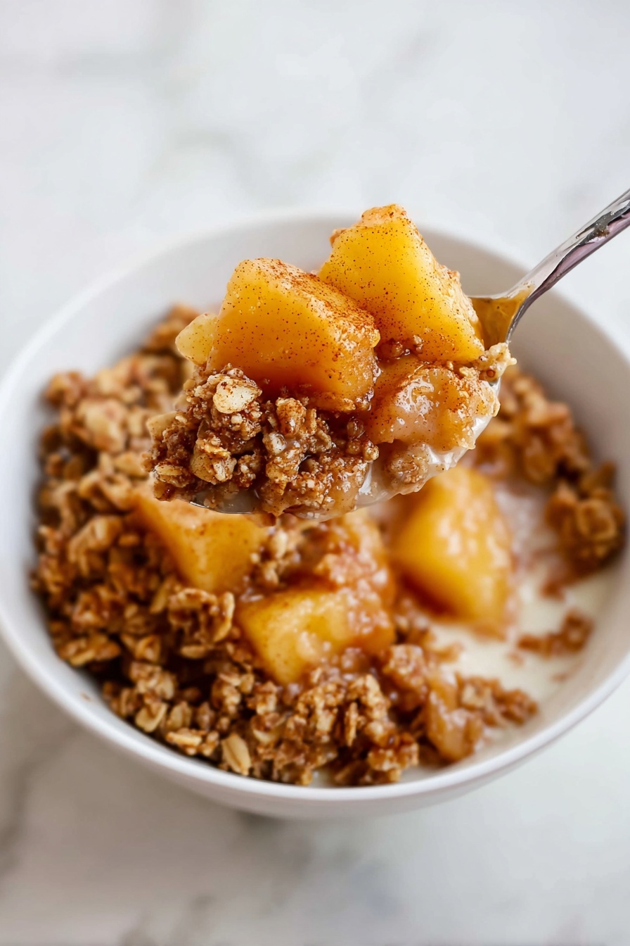 A white bowl filled with a layered dessert of breakfast granola and soft cooked fruit pieces. The bottom layer has light brown granola clusters with a crunchy texture. On top, there are chunks of yellowish-orange cooked fruit, likely pears or apples, coated with a light cinnamon dusting. A spoon scoops a mix of both the soft fruit and granola from the bowl, held close to the camera. The background surface is a white marbled texture. Photo taken with an iphone --ar 2:3 --v 7 - Healthy Apple Crumble Breakfast, healthy apple crumble, nutritious breakfast ideas, quick healthy breakfast, easy apple crumble recipe