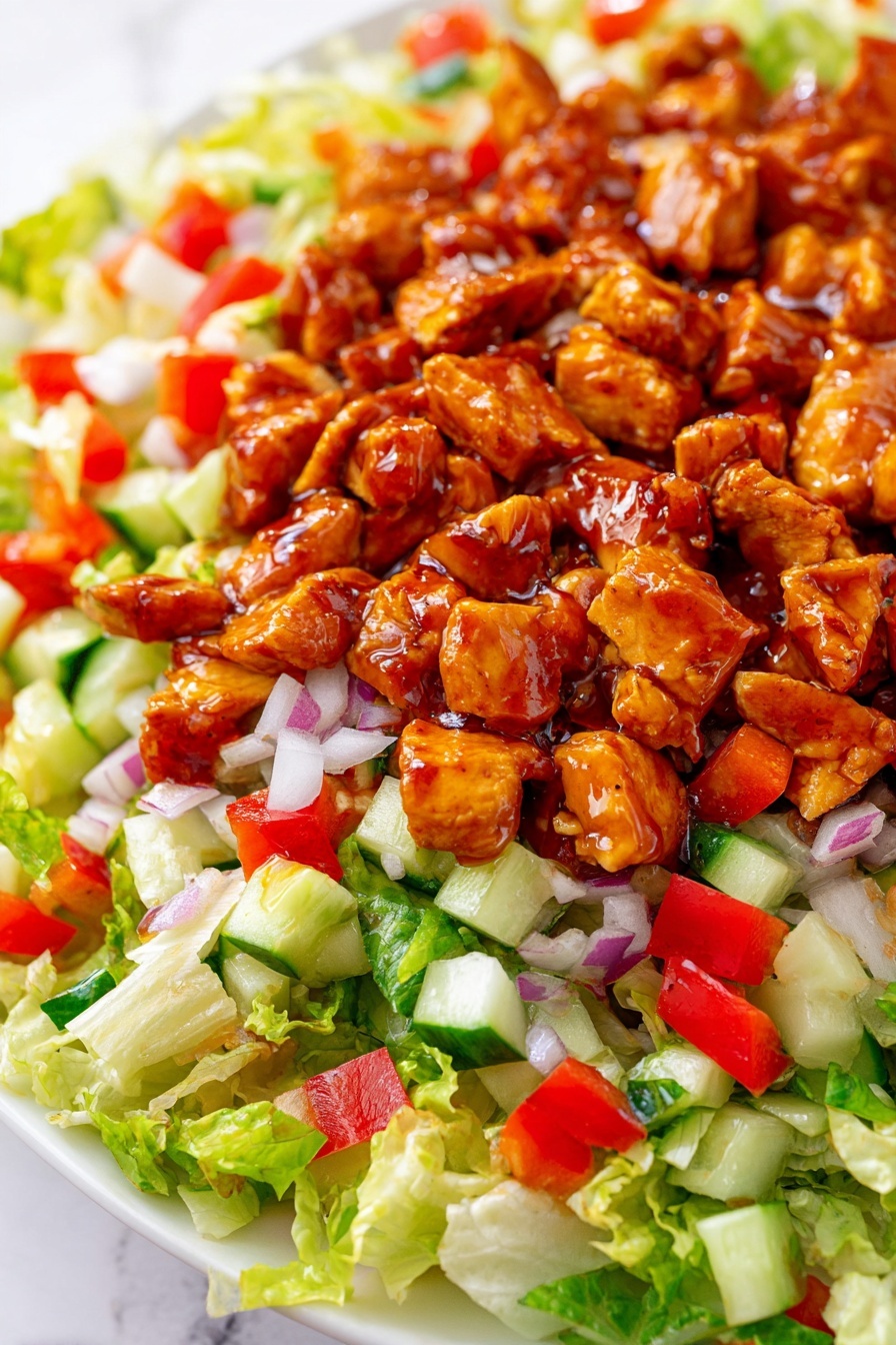 The dish shows a close-up of a salad on a white plate with a white marbled background. The bottom layer has bright green chopped lettuce with a light, crisp texture. Over the lettuce, there are small diced pieces of red bell pepper and white chopped onion spread evenly, adding red and white colors. There are also small cubes of green cucumber scattered throughout this layer. Finally, the top layer consists of chunks of chicken coated in a shiny reddish-brown sauce, giving the salad a rich, glazed look. Photo taken with an iphone --ar 2:3 --v 7 - Honey Hot Chicken Salad, spicy honey chicken salad, quick chicken salad recipe, easy chicken salad, flavorful summer salad