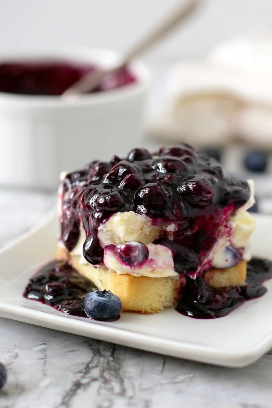 The image shows a small dessert on a white square plate on a white marbled surface. The dessert has two main layers of light golden cake, between which there is a creamy white filling mixed with some purple blueberry syrup. On top, a thick layer of dark purple blueberry sauce with whole blueberries covers the cake, dripping down the sides and pooling on the plate. In the background, there is a blurred white bowl with more dark purple blueberry sauce and a spoon. The scene has a soft natural light. photo taken with an iphone --ar 2:3 --v 7 - Blueberry Syrup for Pancakes and Ice Cream, blueberry syrup recipe, homemade blueberry syrup, easy blueberry syrup, fruit topping for desserts